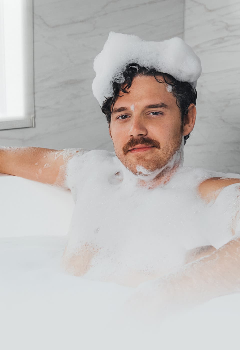 Male model sitting in a bathtub covered in suds