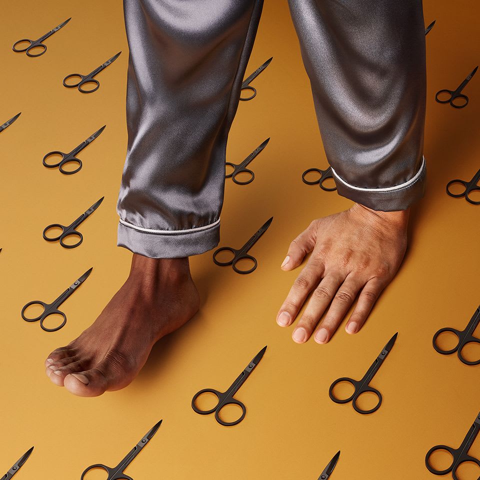 The Shears 3.0 cuticle scissors laying on the ground in a tiled format next to male models foot and hand