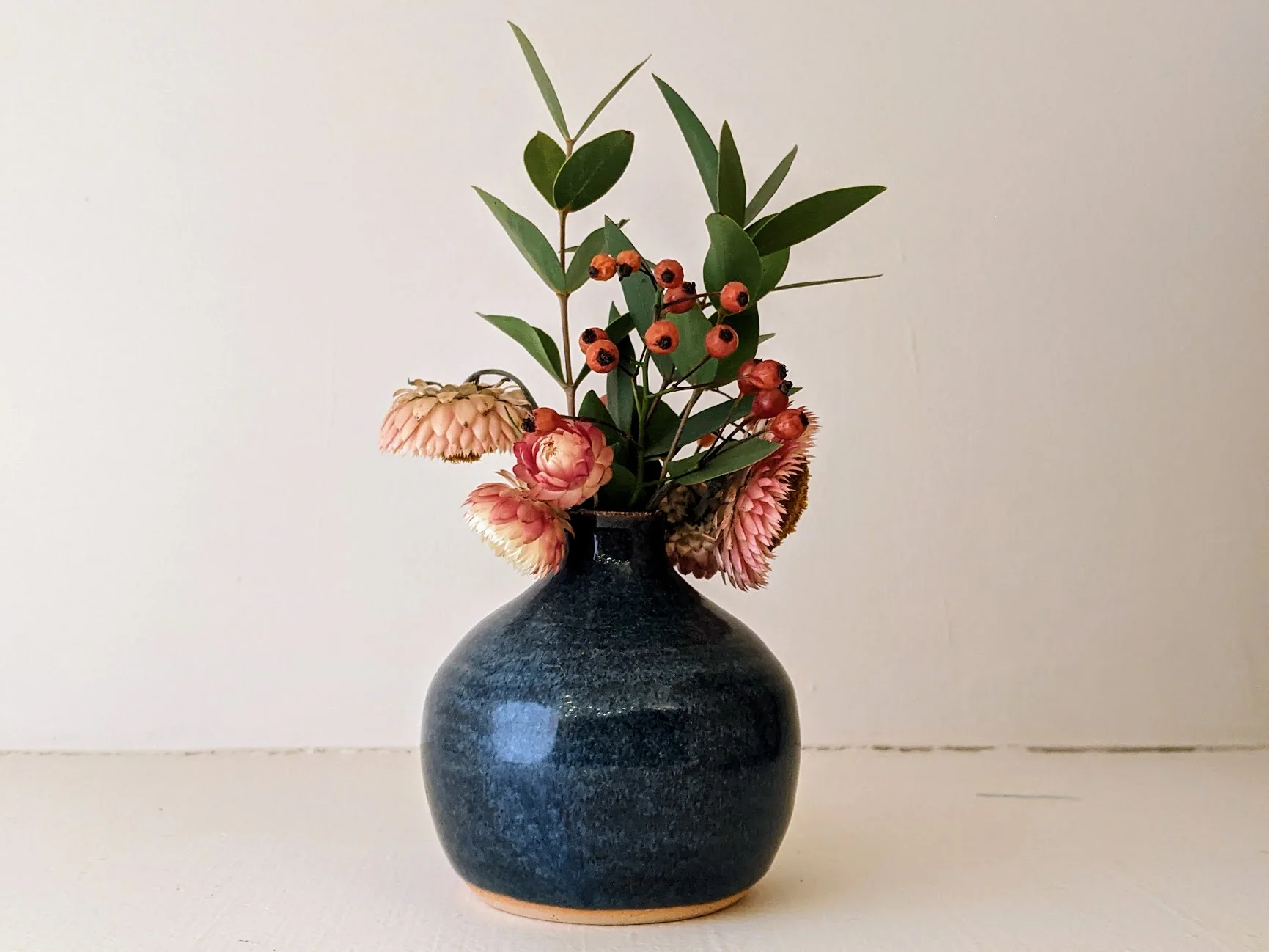 Blue bud vase with dried pink flowers in it.