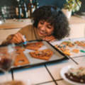 Woman leaning over baking tray icing unassembled pieces of Gingerbread house