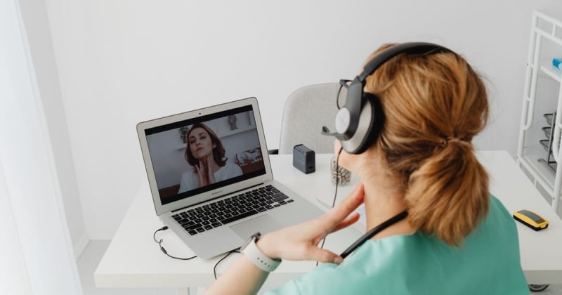Woman in medical scrubs having a telemedicine session using a laptop from home.