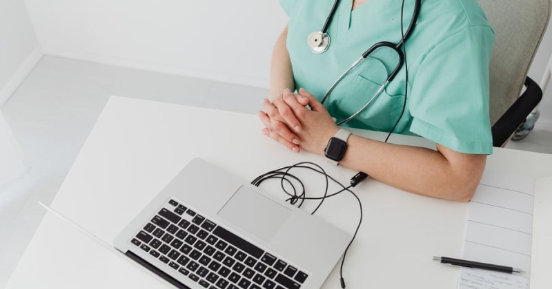 Doctor in scrubs with stethoscope conducting online consultation using a laptop.