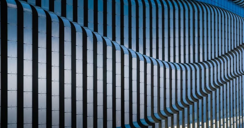 Close-up of a modern building facade featuring wave-like metallic structures and a monochromatic color scheme.