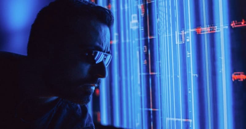 A man in sunglasses intently studies a vibrant blue holographic screen, symbolizing digital technology.