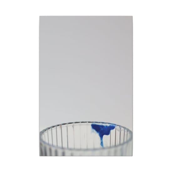 Artistic vertical shot of a glass with a splash of blue paint, offering copy space.