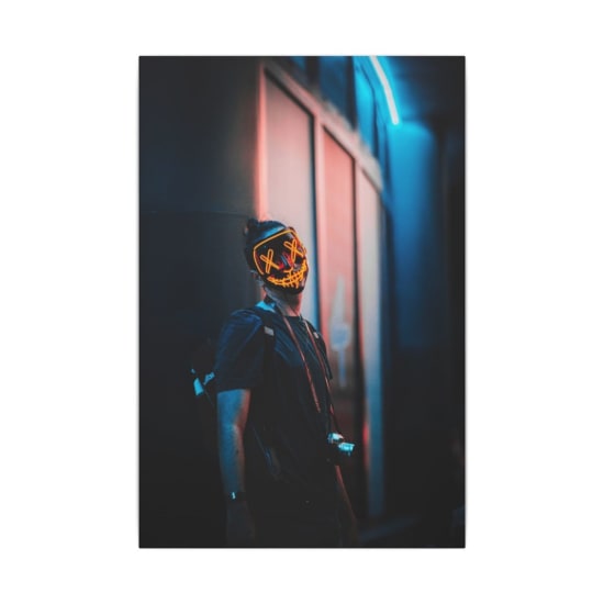 A person wearing a glowing smiley mask stands in a neon-lit urban alley at dusk, capturing cyberpunk aesthetics.