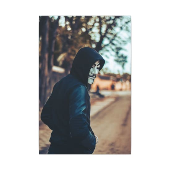 A man in a hoodie wearing a Guy Fawkes mask walks down an urban street, creating an air of mystery and intrigue.