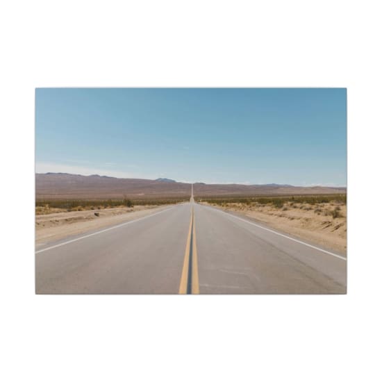 A long, straight road stretches through a vast desert landscape under a bright blue sky.