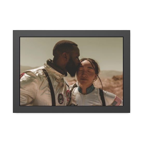 A couple in futuristic space suits share an intimate moment with a desert landscape backdrop.