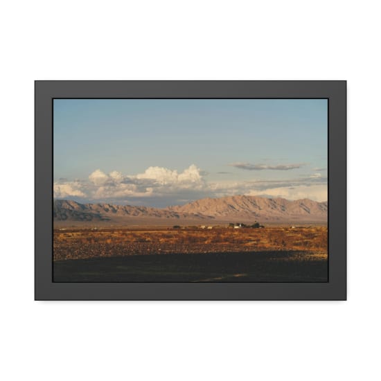 Broad desert vista under a vast sky, featuring distant mountain ranges and scattered clouds.