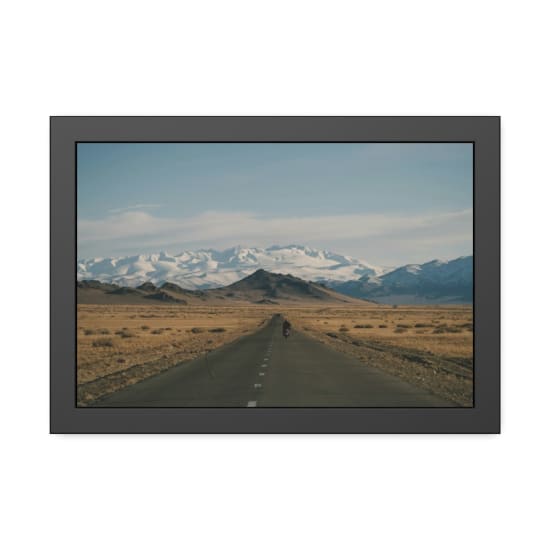 Distant cyclist on a vast highway towards snowcapped mountains in Mongolia.