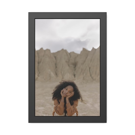 A fashionable young woman with curly hair poses thoughtfully in a striking desert landscape.