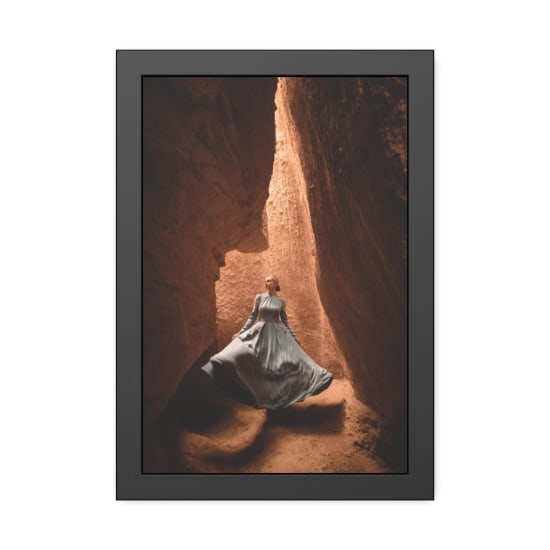 A woman in a gray dress stands gracefully in a narrow rocky canyon, creating an artistic and elegant scene.