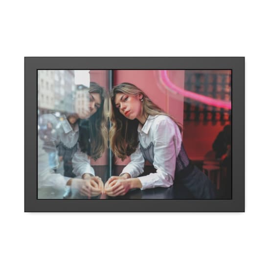 Fashionable woman leaning against a reflective window in a modern urban setting with neon lighting.