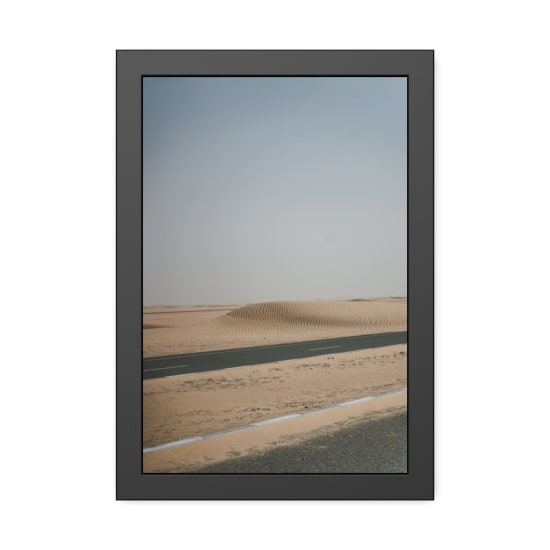 A remote asphalt road cuts through a sandy desert with dunes under a clear sky.