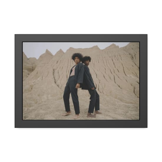 Two fashion models in black attire pose dramatically against a unique desert background.