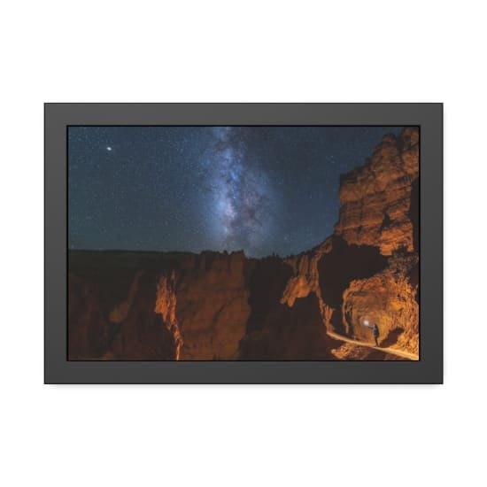 A lone traveler explores Bryce Canyon at night, illuminated by the Milky Way in a clear starry sky.