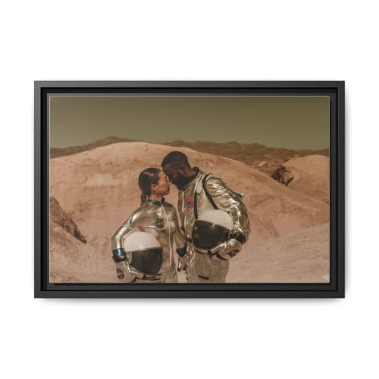A diverse couple in astronaut suits shares an intimate moment in a desert landscape.