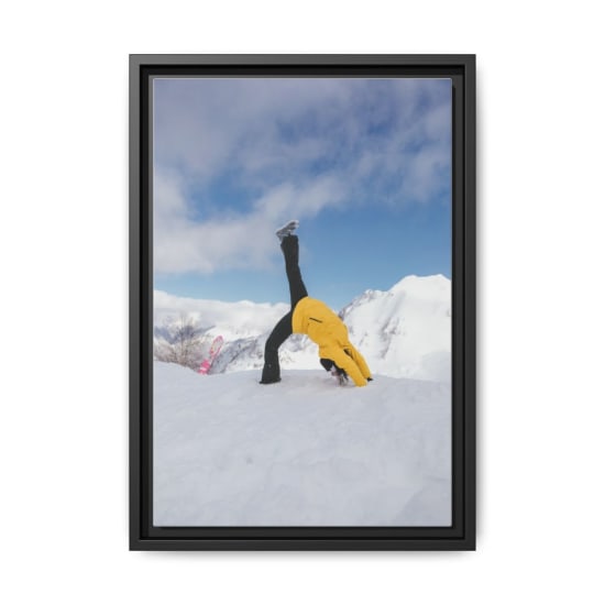 A woman in a yellow jacket does a handstand in snowy mountains, showcasing winter adventure.