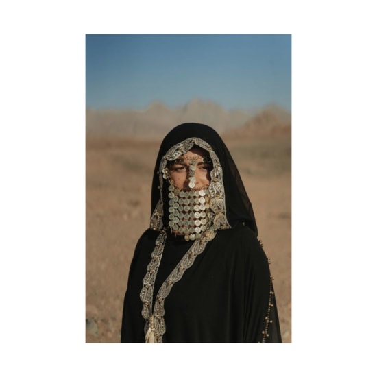 Woman wearing traditional Bedouin attire with coin jewelry in desert landscape.