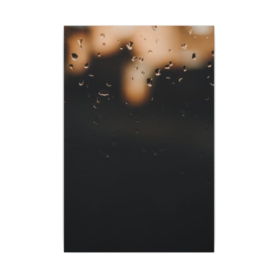 Blurred raindrops on a window with soft evening lights, creating a dreamy atmosphere.