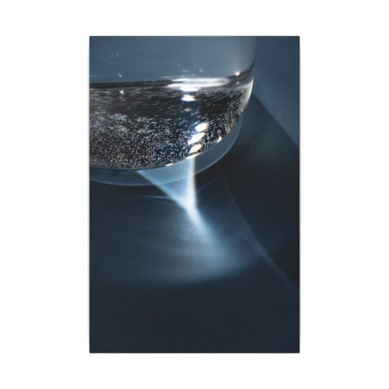 A creative close-up of a glass of water on a blue surface with intriguing light reflections.