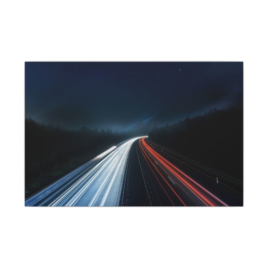 Long exposure night shot capturing stunning red and white light trails on a highway under a starry sky.