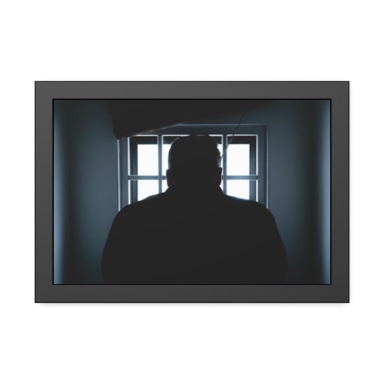 Dark silhouette of a man in a prison cell, backlit by window bars.