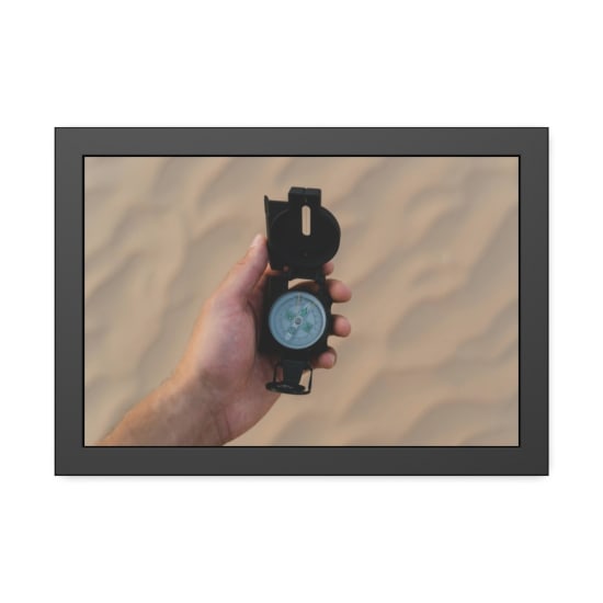 Hand holding a compass over sandy desert terrain, symbolizing navigation and adventure.