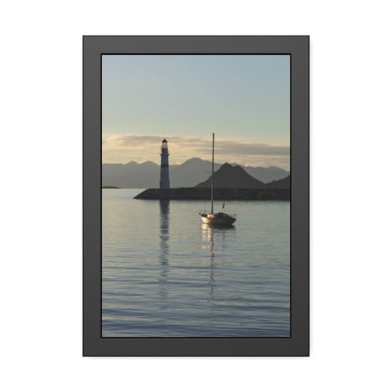 Tranquil scene of a sailboat near a lighthouse with mountain backdrop at sunset.
