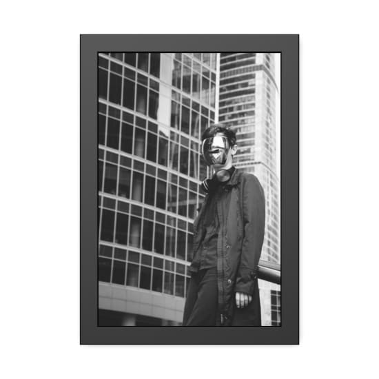 Black and white photo of a person wearing a reflective mask in a cityscape.