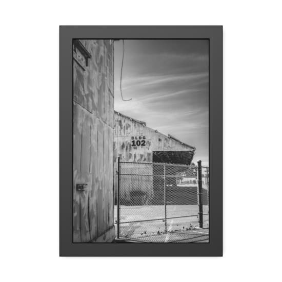 Black and white photo of an abandoned industrial building with a chain link fence, labeled BLDG 102.