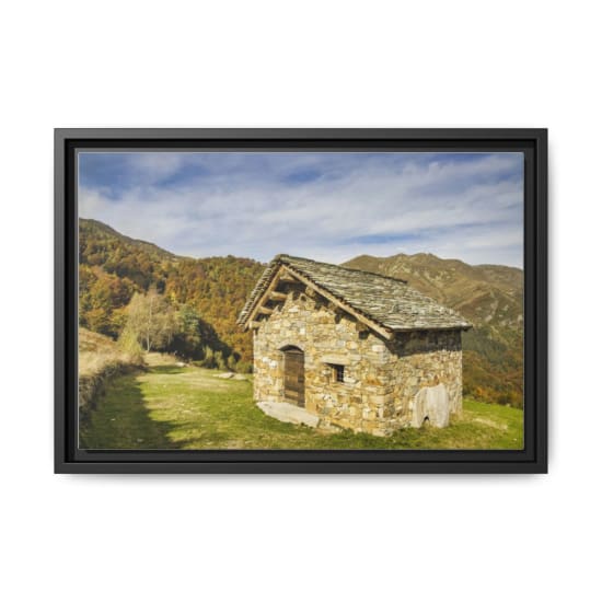 A rustic stone cabin nestled in a colorful autumn mountain landscape under a blue sky.