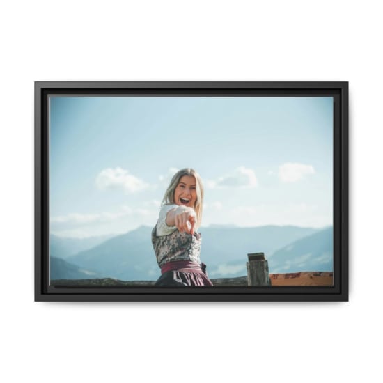 Blond woman in a traditional dirndl pointing joyfully with mountains in the background.
