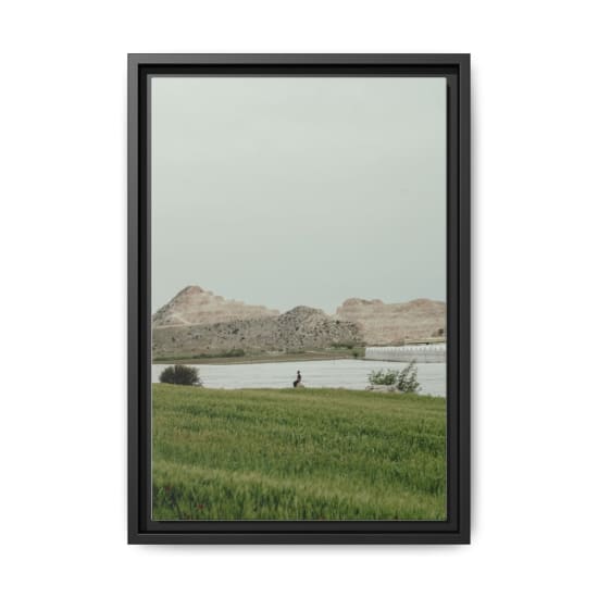 A tranquil landscape featuring a lush field, a calm river, and scenic hills under an overcast sky in Adana, Türkiye.