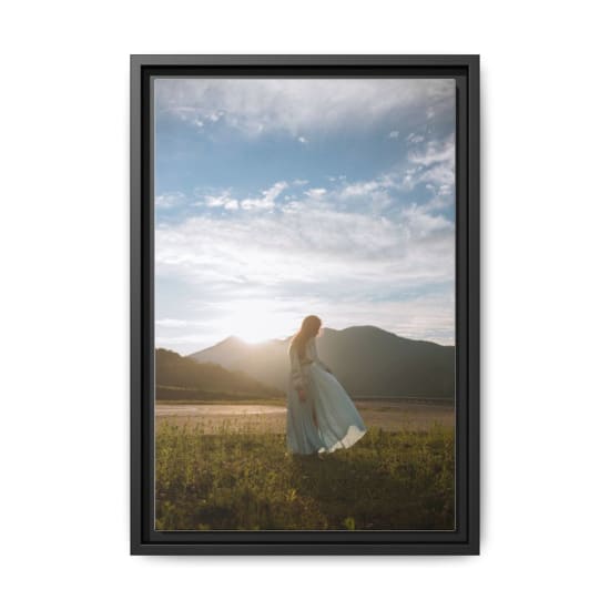 A serene outdoor scene featuring a woman in a flowing blue dress, backlit by the sun with mountains in the background.