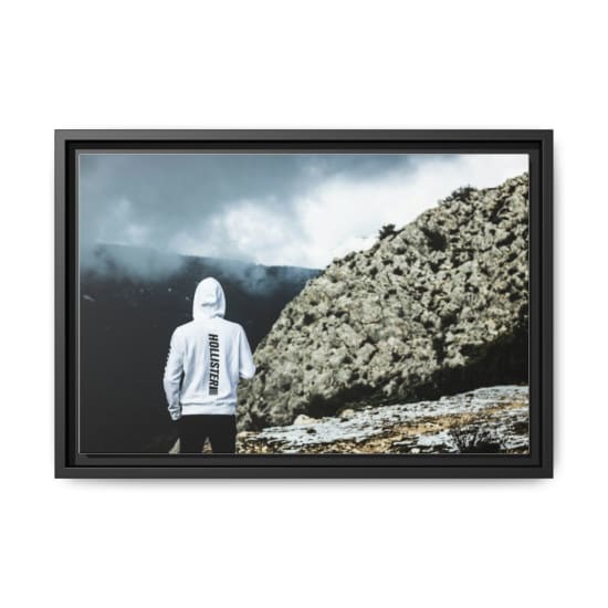 A man in a white hoodie stands facing rocky mountains under dramatic clouds.