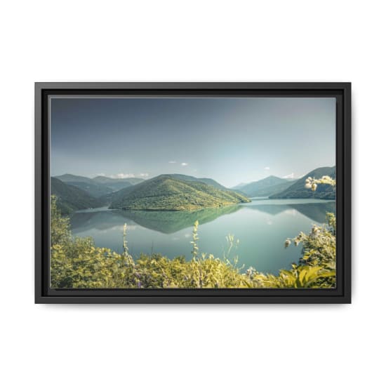 Tranquil lake surrounded by lush green mountains under a clear summer sky.