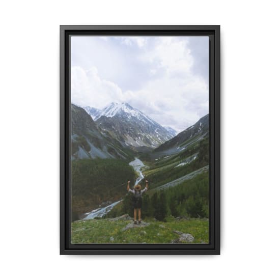 Hiker celebrating atop a mountain with breathtaking views of a lush valley and snow-capped peaks.
