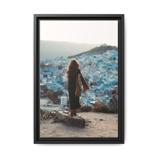A woman stands on a hill overlooking Chefchaouen's iconic blue buildings at sunset.