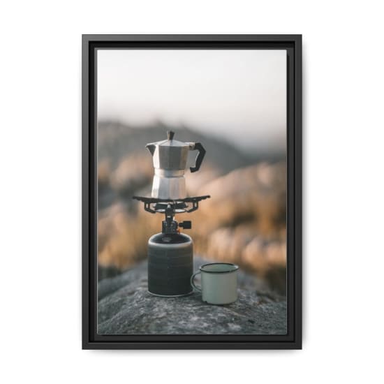 A coffee maker brews fresh coffee on a camping stove in a mountainous landscape.