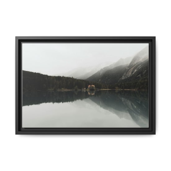 Serene lake scene reflecting dense forest and mountains under overcast skies.
