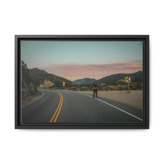 A woman walks along a winding mountain road under a vibrant sunset sky, offering a sense of adventure and tranquility.