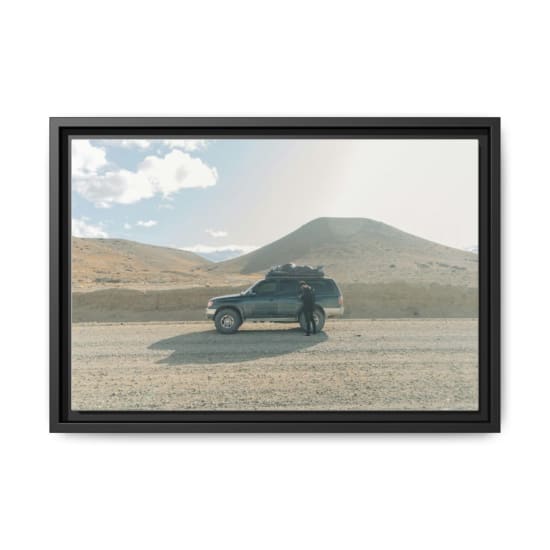 Man standing by SUV on a gravel road in Argentina's desert landscape, enjoying a road trip.
