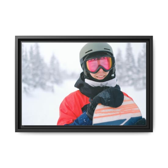 A snowboarder in winter gear smiling while holding a snowboard in snowy landscape.