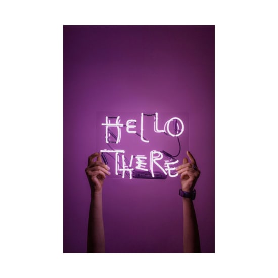 Bright neon sign saying 'Hello There' held by hands against a purple background.