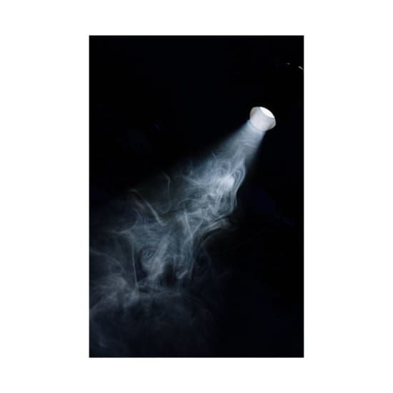A beam of light penetrates through smoke in a dark setting, creating a moody atmosphere.