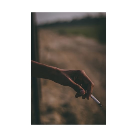 Artistic image of a hand holding a cigarette outdoors with a blurred background, evoking a moody atmosphere.