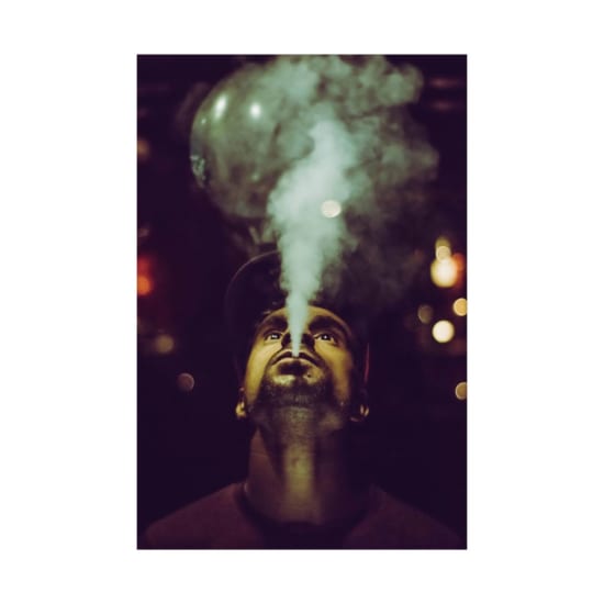 Low-angle portrait of a man vaping at night with artistic bokeh effects in the background.