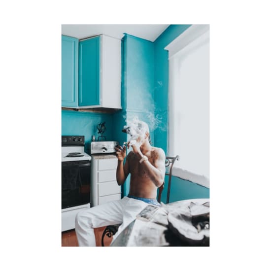 Shirtless man with tattoos smoking indoors, captured in a colorful kitchen setting.